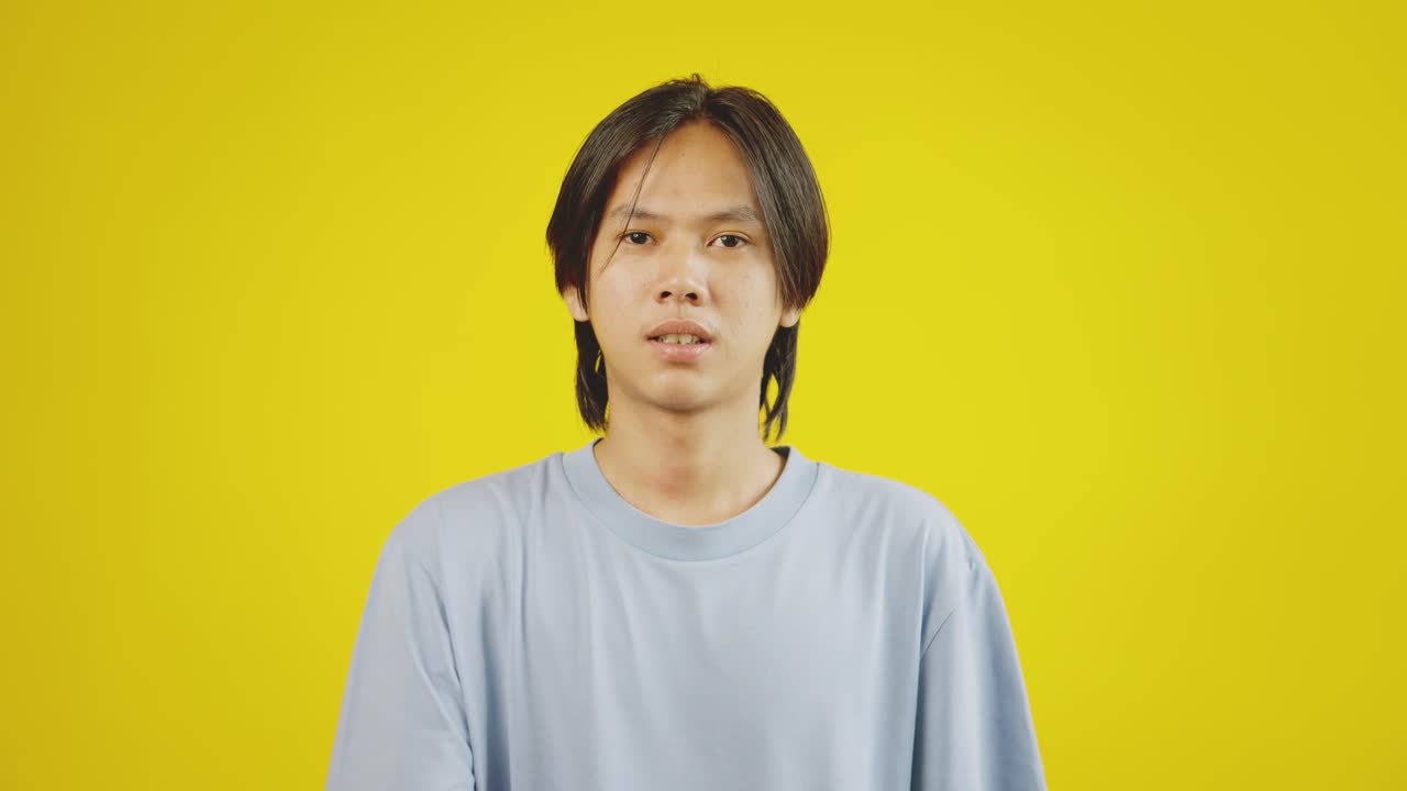 젊은 아시아인 남자가 노란색 배경 위에 고립 된 화면에 같은 버튼으로 휴대 전화를 가리키고 있습니다.