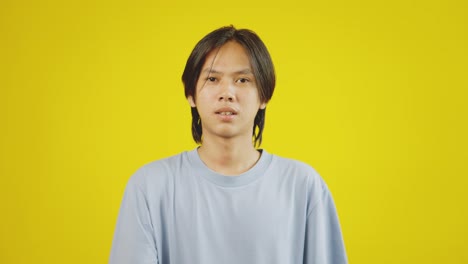 young asian man pointing at mobile phone with like button on screen isolated over yellow background