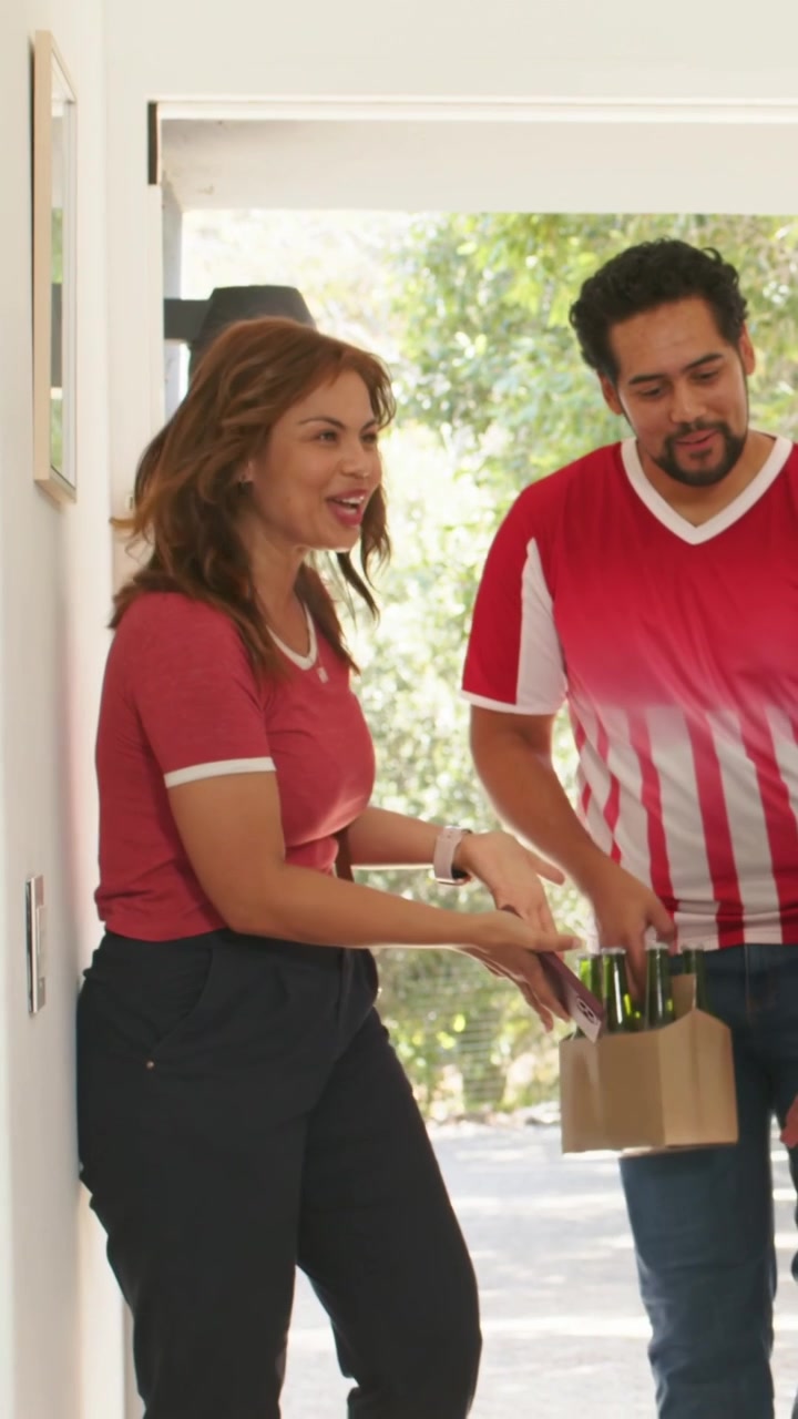 Coppia che arriva alla porta e saluta l'ospite: donna con maglietta rossa che saluta con il telefono, uomo con maglia a righe che consegna un trasportino