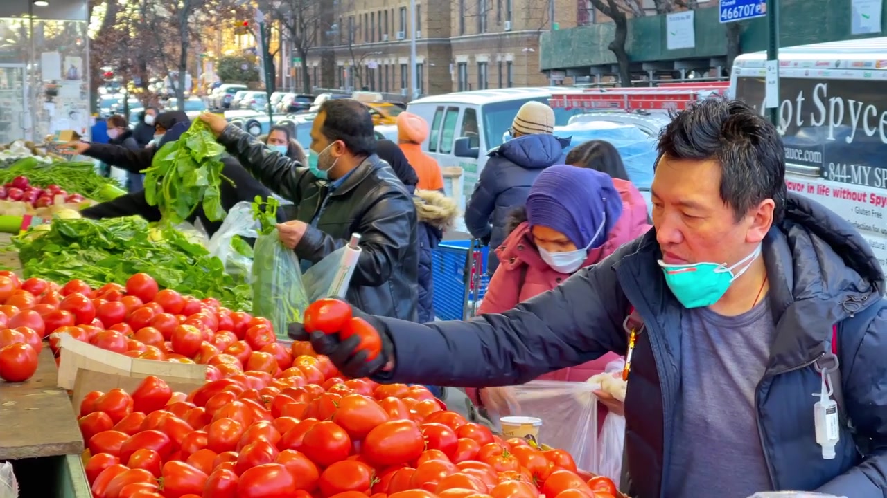 New York, ABD, 9 Mart 2022: Müşteriler kaldırımda sergilenen ürünlerden domates seçiyor. Açık hava sebze-meyve tezgahında domates seçen müşterilerin, maskelerin ve park etmiş bir minibüsün yakın sokak seviyesi görünümü