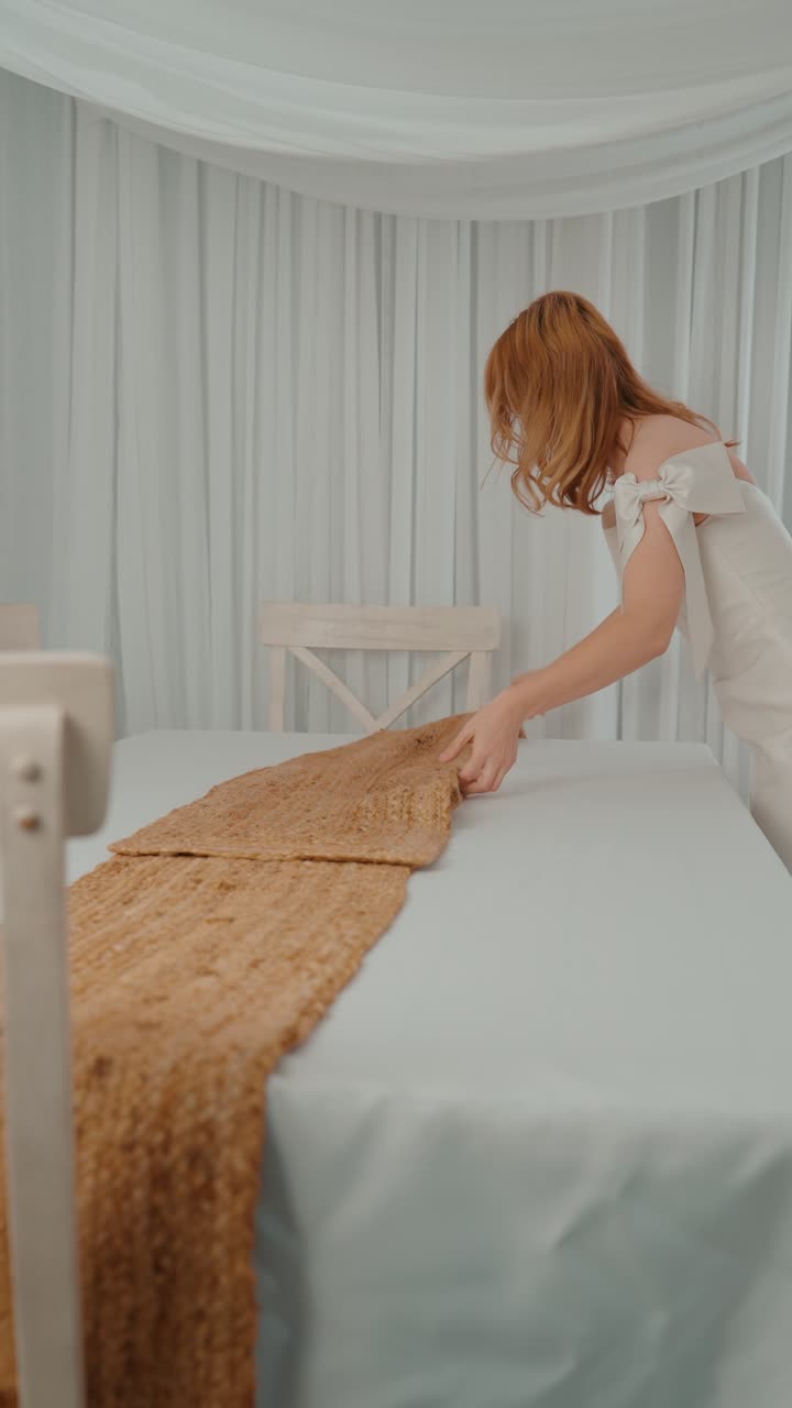 vista lateral de una mujer rubia arreglando una elegante mesa blanca en un interior suave y aireado