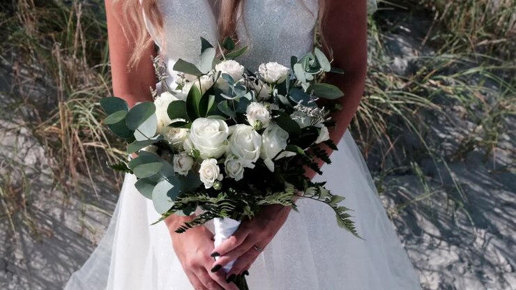 Bride holding a bridal bouquet of roses and eucalyptus on the beach