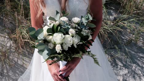 bride holding a bridal bouquet of roses and eucalyptus on the beach