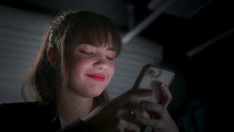 happy young woman receiving a text message on her smartphone at night