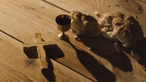 concepto religioso filmado con cáliz cruz de pan roto y vino en una mesa de madera con un charco de luz