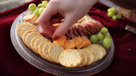 nahaufnahme einer weiblichen hand, die draußen am strand ein köstliches picknick-dinner mit wurstwaren zubereitet