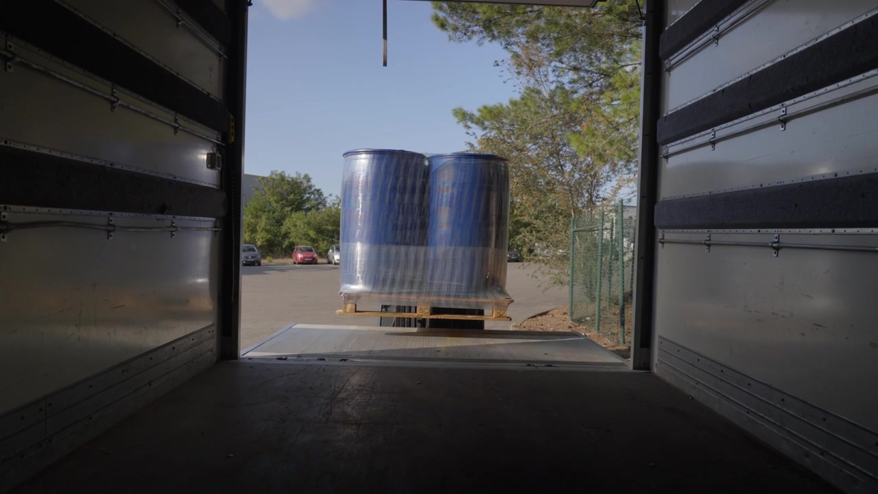 Gaffeltruck læsser blå industritønder op på en lastbils lift. Professionel logistik og fragt på et fabriksområde.