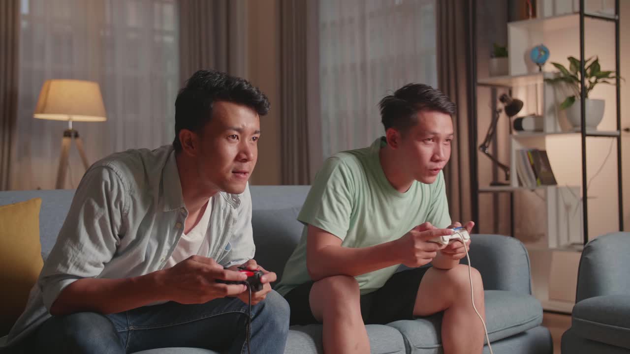 Asian Friends Playing Video Games At Home. Male Happy To Win Victory And Another Man Feeling Disappointed