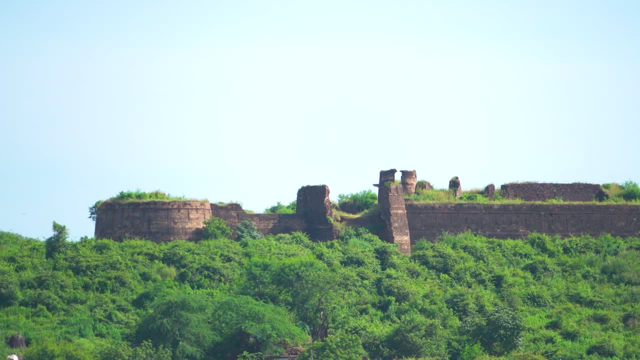 fotografía de cerca de una antigua fortaleza o castillo abandonado y cubierto de denso bosque verde en la cima de una colina en madhya pradesh, india