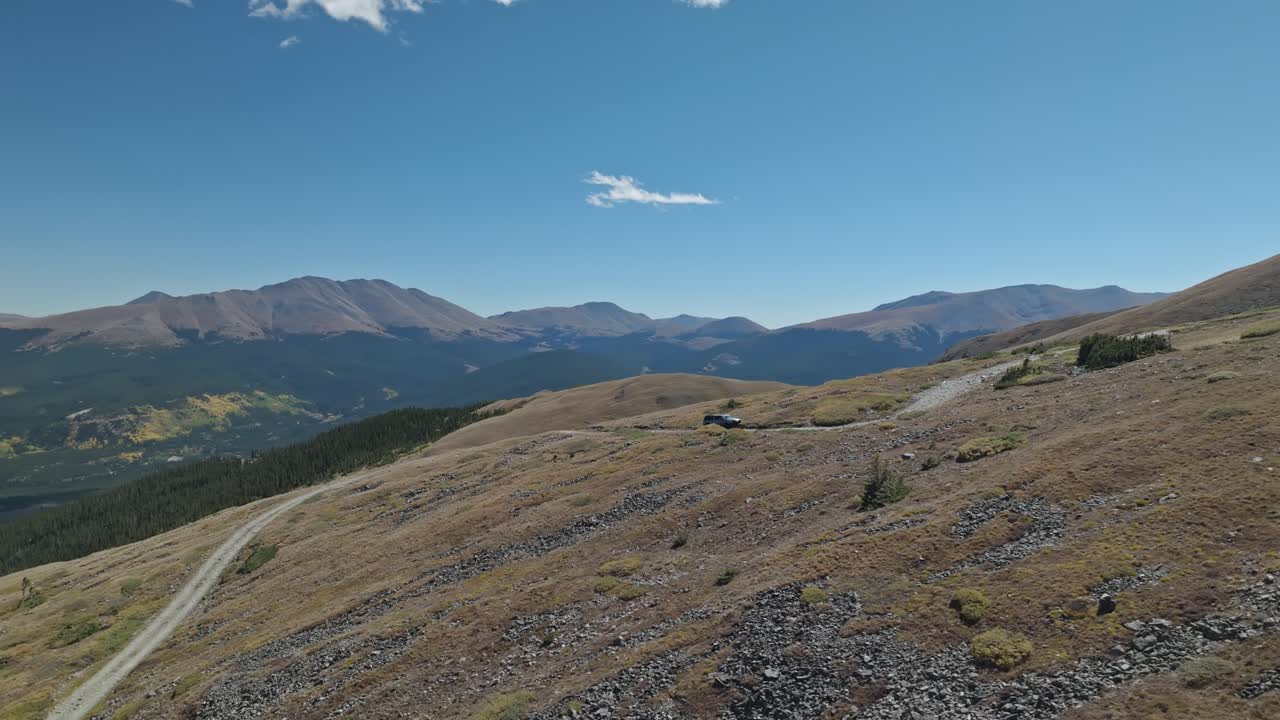 Aerial panoramic orbit as car drives along winding dirt path in the Rocky Mountains Peak 10 trail Breckenridge Colorado