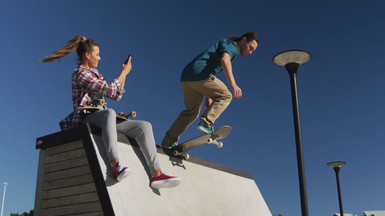 mujer caucásica feliz tomando una foto de su amigo masculino patinando