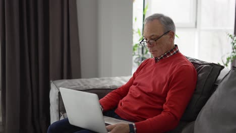 Alter-Mann-Genießt-Seine-Freizeit,-Während-Er-Einen-Laptop-Auf-Dem-Sofa-Benutzt
