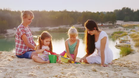 Zwei-Damen-Spielen-Mit-Den-Kindern-Im-Sand-Vor-Der-Kulisse-Eines-Wunderschönen-Sees,-An-Dem-Touristen