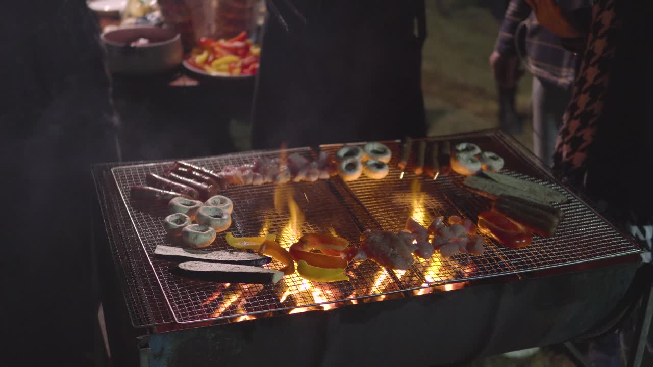 Persone in piedi davanti al barbecue che grigliano funghi, salsicce, pollo, melanzane di fronte alla casa in un giardino.