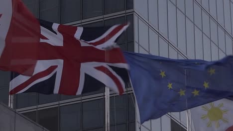 Vereinigtes-Königreich-Union-Jack-Und-Flagge-Der-Europäischen-Union-An-Einem-Windigen,-Stürmischen-Tag-Gegen-Den-Brexit-Des-Geschäftszentrums