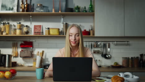 Girl-greeting-online-conference-sitting-at-kitchen-while-man-dancing-on-backdrop