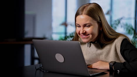 resilient smiling woman working on computer pulls closer to the screen. lady rejoicing looking at her laptop rising hands cheerfully.