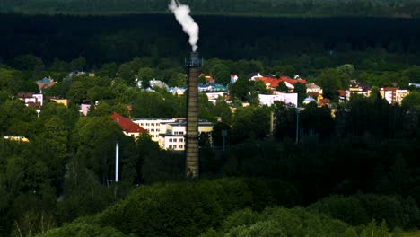 Industrial-chimney-white-smoke-aerial-view-with-surrounded-green-forest-and-small-town