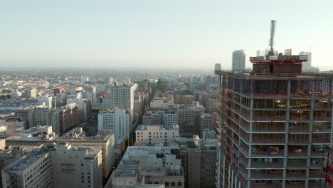 Construction-Site-on-Skyscraper-Tower-in-Downtown-Los-Angeles,-California-Skyline-in-Beautiful-Sunset-light,-City-in-development,-Scenic-Aerial-Dolly-left