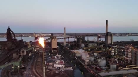 Zug-Island-Steel-Factory,-Steel-mill-in-Detroit,-Michigan-aerial-panning-shot-with-burning-chimney-at-twilight