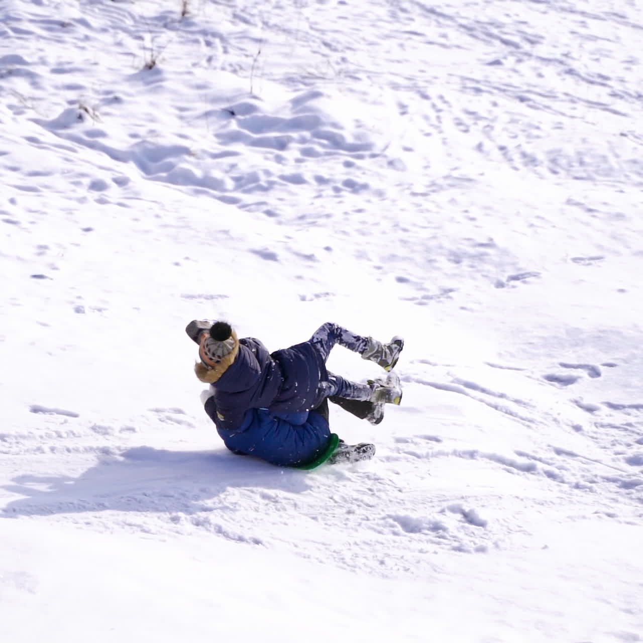 Child boy having fun, riding from a hill. Frost winter season.Cute little boy with saucer sleds outdoors on winter day and hits his friend or sister or brother, ride down the hills, winter games and fun. Two children hit while sledging.