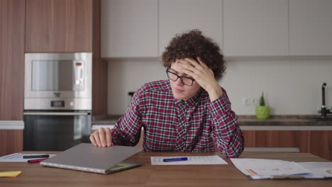 brooding serious curly freelancer man sit at table in comfortable home office room work on laptop looks concentrated thinking over business issue solution makes telecommute job