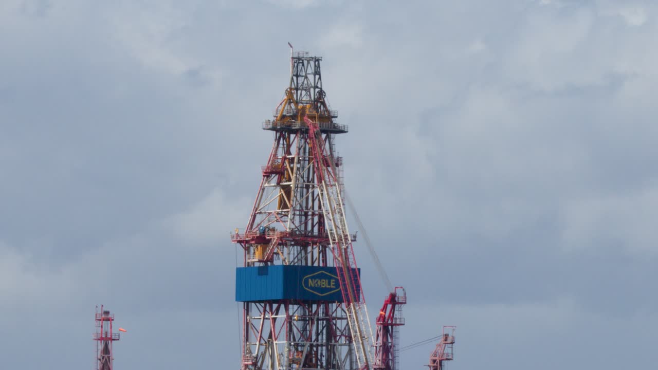 Large offshore oil rig moves closer to Cromarty, Scotland, under cloudy skies, telephoto perspective
