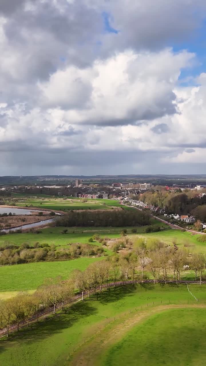 Veduta aerea di campi verdi, fiume e città lontana sotto un cielo nuvoloso