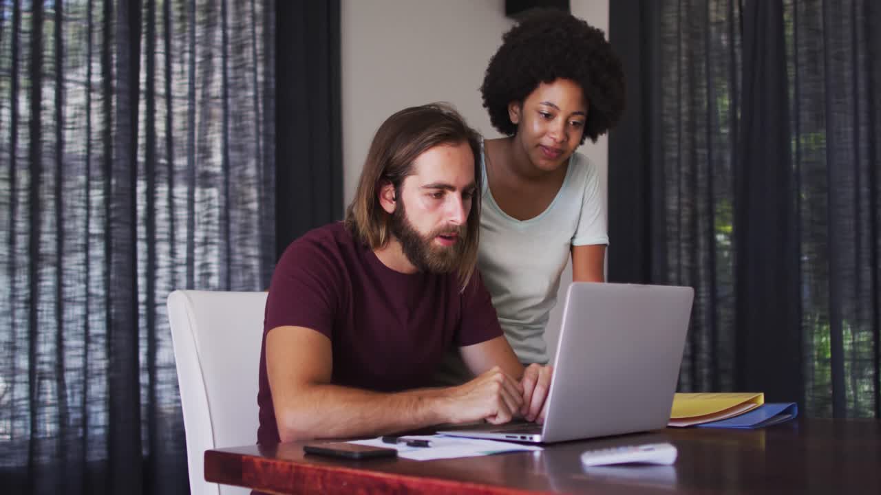 Mixed race couple using laptop and high fiving each other at home