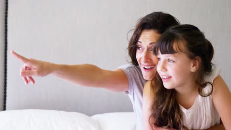 Mother-with-daughter-pointing-at-a-distance-on-bed