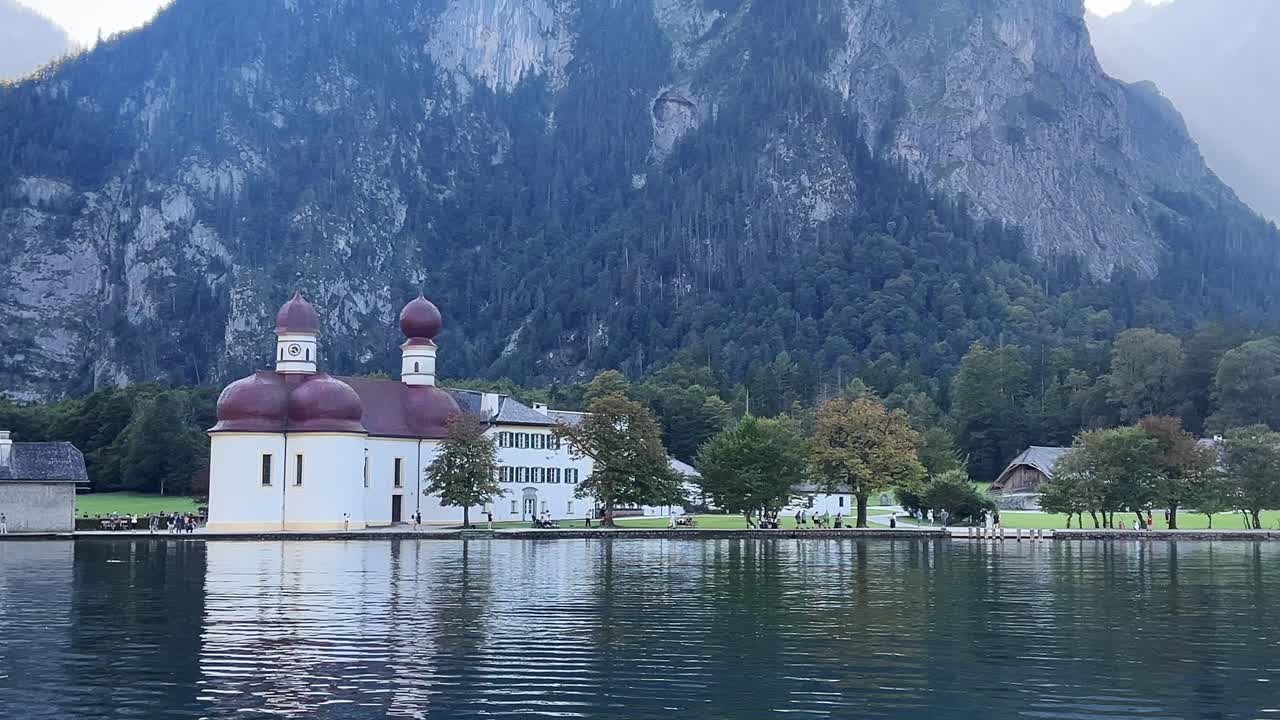 Die St.-Bartholomäus-Kirche am Ufer des Königssees in Berchtesgaden, Deutschland. Ruhiges Alpenwasser spiegelt die historische Kirchenarchitektur und die steilen bewaldeten Berge wider