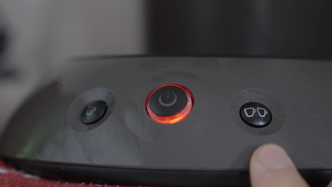 Close Up of Finger Power Button on Modern Pod Coffee Machine with Red Light