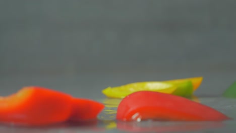 rodajas frescas y multicolores de pimientos cayendo, salpicando agua, primer plano