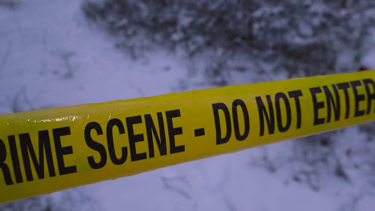 Yellow crime scene tape in sharp focus over a snowy forest road, creating a tense investigation mood with soft winter bokeh