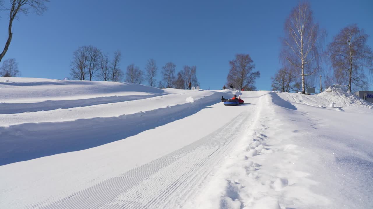 Slow motion shot of a ski resort, man and his daughter sledding on the snowy track