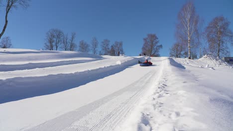 Slow-motion-shot-of-a-ski-resort,-man-and-his-daughter-sledding-on-the-snowy-track