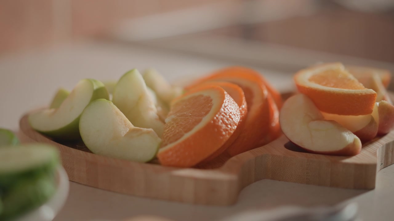 Vista ravvicinata di spicchi di mela affettati e pezzi d'arancia su un tagliere di legno accanto al piano di lavoro della cucina, con texture lucida della frutta, luce calda e uno sfondo sfocato e morbido.