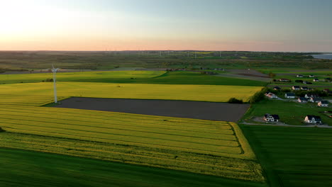 Vista-Aérea-De-Extensos-Campos-Con-Una-Sola-Turbina-Eólica-En-Primer-Plano-Y-Muchas-Más-Turbinas-Salpicando-El-Horizonte.