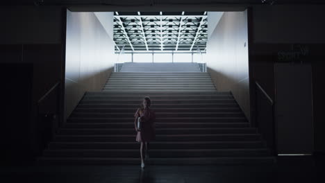 Worried schoolgirl walk down empty stairway alone. Girl enter dark corridor.