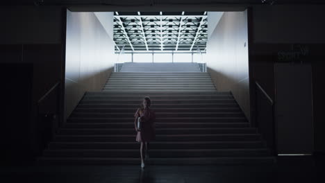 worried schoolgirl walk down empty stairway alone. girl enter dark corridor.