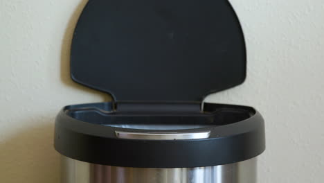 man throws away paper towel in motion sensing touchless trash can - close-up