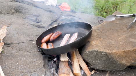 a close up shot of sausages and bacon being cooked in a pan over a camp fire in rural africa