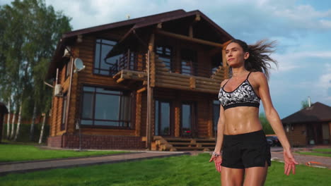 mujer delgada y hermosa en ropa deportiva en el fondo de la casa en el césped realiza saltos para el entrenamiento cardiovascular y la quema de grasa