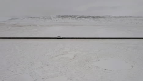 Aerial:-Following-a-car-from-the-right-side,-driving-on-a-snowy-road