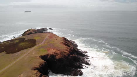 Aerial-drone-view-overlooking-people-at-the-Look-At-Me-Now-Headland-bay,-near-Emerald-Beach,-in-Australia