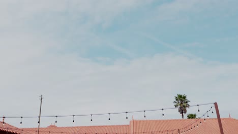 decorative hanging lights stretch across rooftops with blue sky and palm tree in background