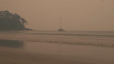 lone boat in ocean water surrounded by smoke from nearby bushfire, bruny island, tasmania, australia