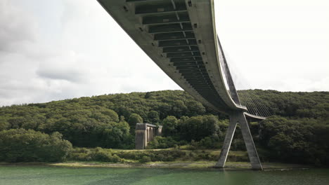 lateral arc under a large suspension bridge over body of water seen from under