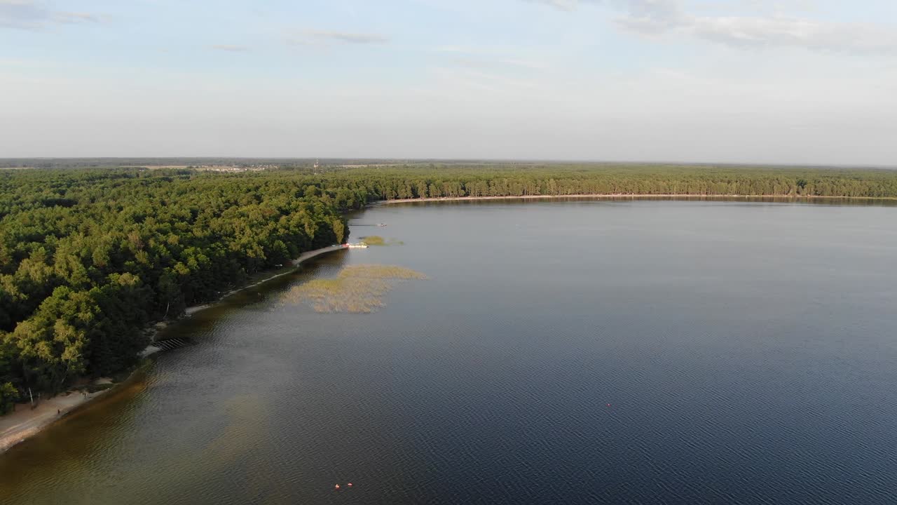 Vista aérea de um lago durante uma noite de verão com floresta densa ao fundo.
