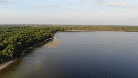 Vista-Aérea-De-Un-Lago-Durante-Una-Noche-De-Verano-Con-Un-Denso-Bosque-En-El-Fondo